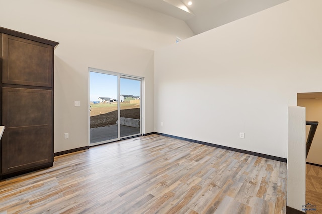 spare room with baseboards, high vaulted ceiling, and light wood-style floors