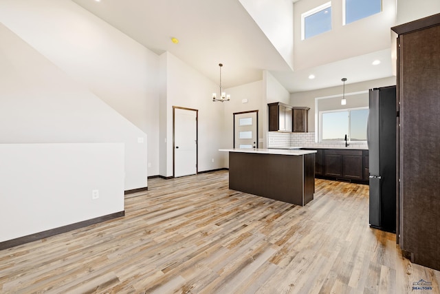 kitchen with light countertops, a kitchen island, freestanding refrigerator, light wood-style flooring, and dark brown cabinets