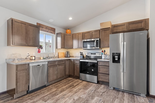 kitchen with vaulted ceiling, recessed lighting, wood finished floors, a sink, and stainless steel appliances