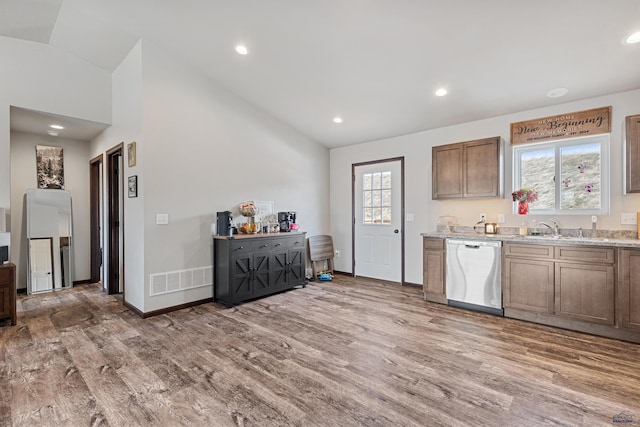 kitchen with light wood-style flooring, stainless steel dishwasher, a sink, and vaulted ceiling