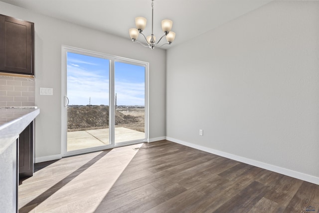 unfurnished dining area featuring dark wood-style flooring, baseboards, and an inviting chandelier