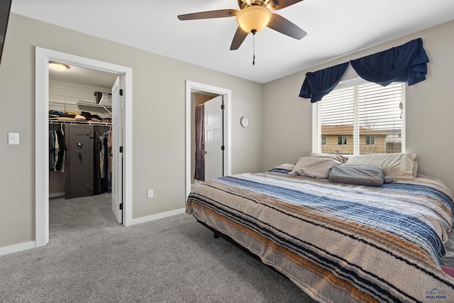 carpeted bedroom featuring a closet, ensuite bath, a ceiling fan, a walk in closet, and baseboards