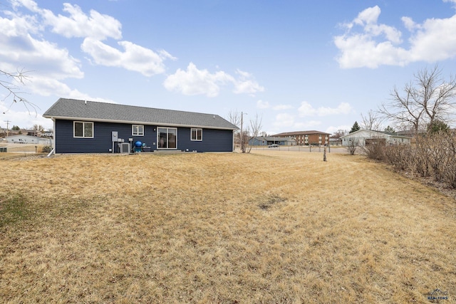 rear view of property featuring central AC, a lawn, and roof with shingles