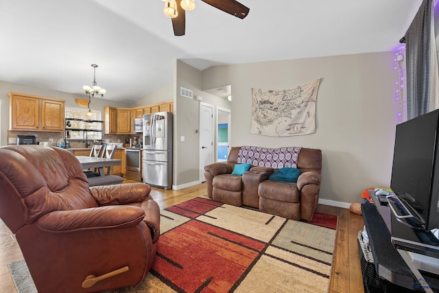 living room featuring light wood-style floors, ceiling fan with notable chandelier, visible vents, vaulted ceiling, and baseboards