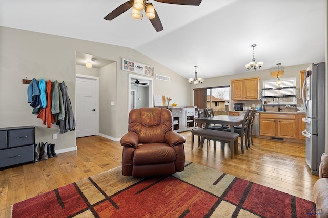 living area with visible vents, baseboards, light wood-style floors, vaulted ceiling, and ceiling fan with notable chandelier