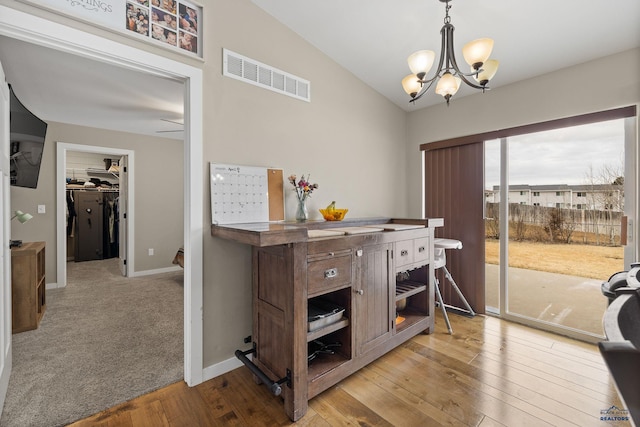 interior space featuring light wood-style flooring, vaulted ceiling, visible vents, baseboards, and a notable chandelier