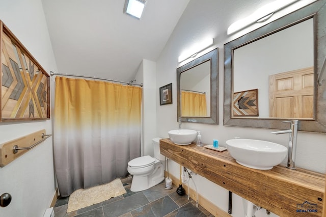 full bath featuring stone finish floor, a shower with curtain, toilet, lofted ceiling, and baseboards