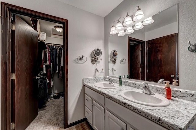 bathroom with a textured wall, double vanity, a sink, and a spacious closet