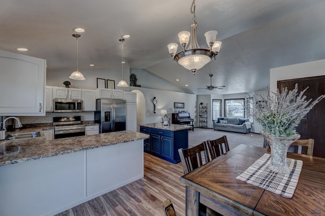 kitchen with ceiling fan with notable chandelier, a peninsula, blue cabinetry, a sink, and stainless steel appliances