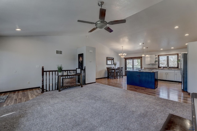 unfurnished living room featuring vaulted ceiling, visible vents, carpet, ceiling fan with notable chandelier, and wood finished floors