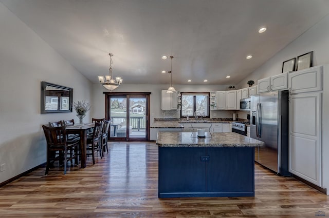 kitchen with appliances with stainless steel finishes, a notable chandelier, a kitchen island, lofted ceiling, and a sink