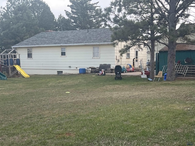 rear view of property with a yard, a shingled roof, and a playground