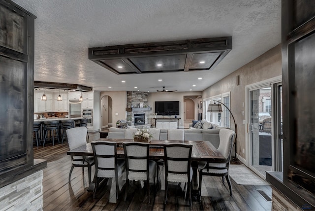 1334 Alta Vista Dr, Rapid City, SD 57701 - dining room featuring arched walkways, a textured ceiling, a ceiling fan, a stone fireplace, and dark wood-style floors