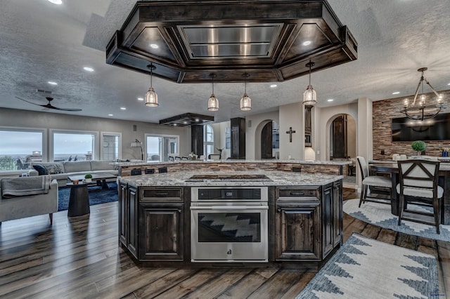 1334 Alta Vista Dr, Rapid City, SD 57701 - kitchen with open floor plan, dark wood-type flooring, stainless steel oven, arched walkways, and ceiling fan with notable chandelier