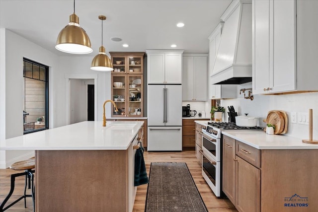 kitchen with white appliances, glass insert cabinets, a breakfast bar, custom exhaust hood, and light wood finished floors