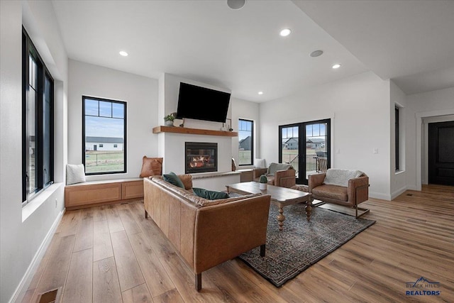 living area featuring light wood-type flooring, baseboards, a glass covered fireplace, and recessed lighting