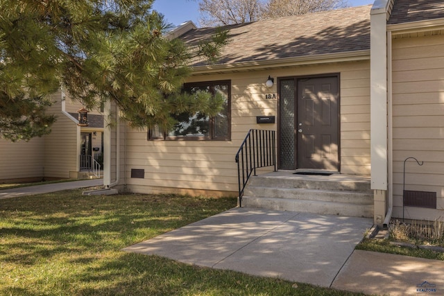 view of exterior entry with a yard and a shingled roof