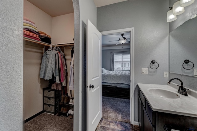 bathroom with ensuite bathroom, a spacious closet, a ceiling fan, a textured wall, and vanity