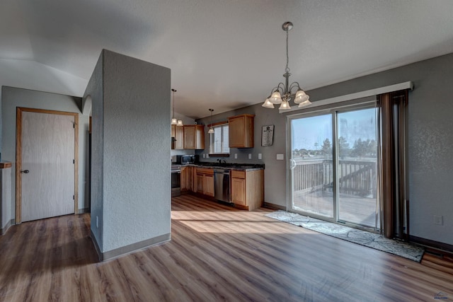 kitchen with vaulted ceiling, a notable chandelier, light wood-style floors, a textured wall, and appliances with stainless steel finishes