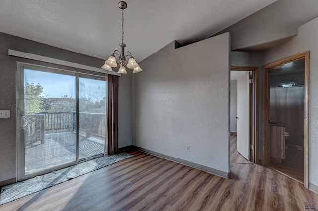 unfurnished dining area with vaulted ceiling, a textured wall, a chandelier, and wood finished floors