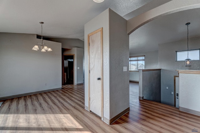 interior space with a textured wall, wood finished floors, arched walkways, and an inviting chandelier