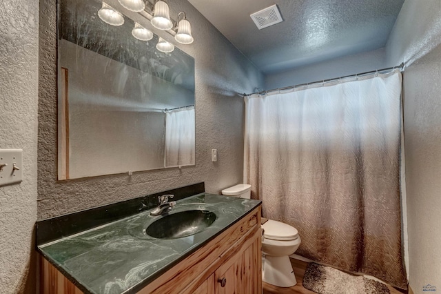 bathroom featuring a textured wall, visible vents, toilet, vanity, and wood finished floors
