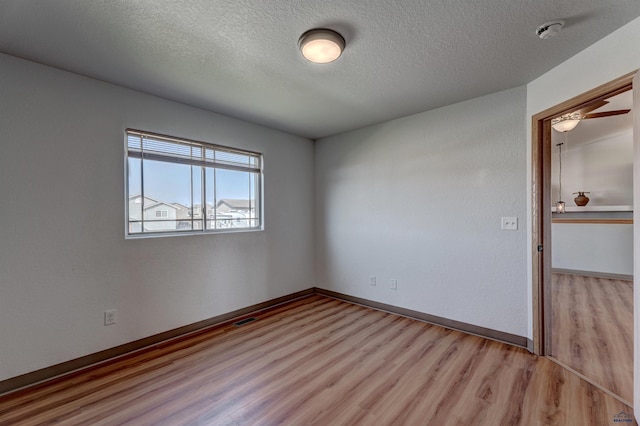 empty room featuring light wood-type flooring, baseboards, visible vents, and a textured ceiling