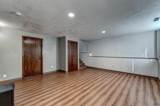 finished below grade area featuring a textured wall, light wood-style flooring, and baseboards