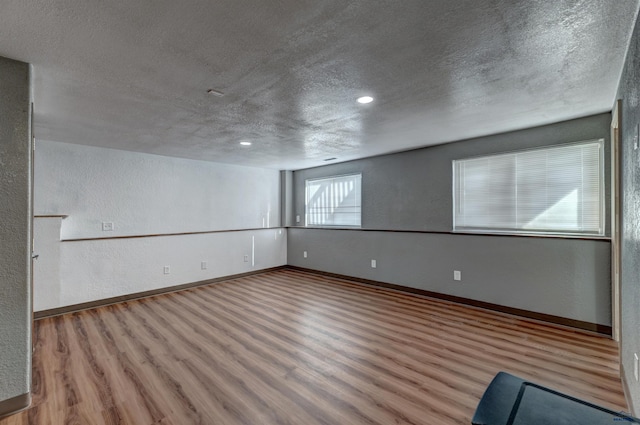 basement with wood finished floors, a textured ceiling, a textured wall, baseboards, and recessed lighting