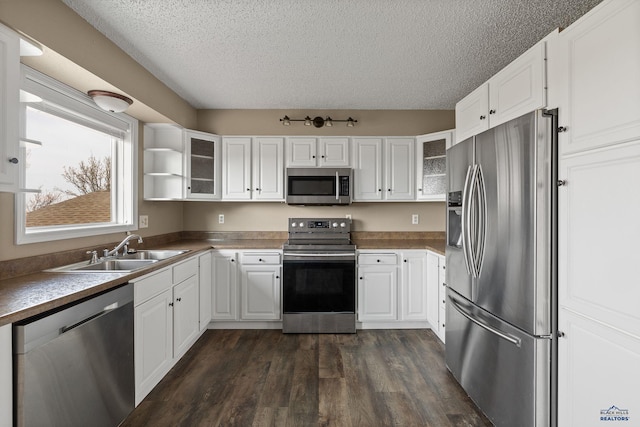 kitchen featuring stainless steel appliances, a sink, a textured ceiling, glass insert cabinets, and dark wood-type flooring