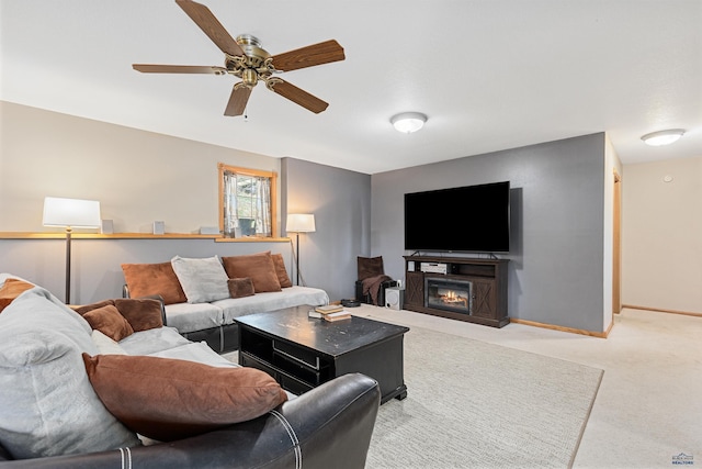 living room featuring baseboards, a ceiling fan, light carpet, and a glass covered fireplace