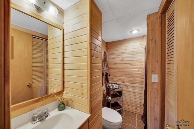 half bathroom with vanity, a closet, toilet, wood walls, and tile patterned flooring