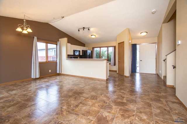 4028 Prairie View Dr, Rapid City, SD 57701 - unfurnished living room featuring a chandelier, rail lighting, stone finish flooring, baseboards, and lofted ceiling