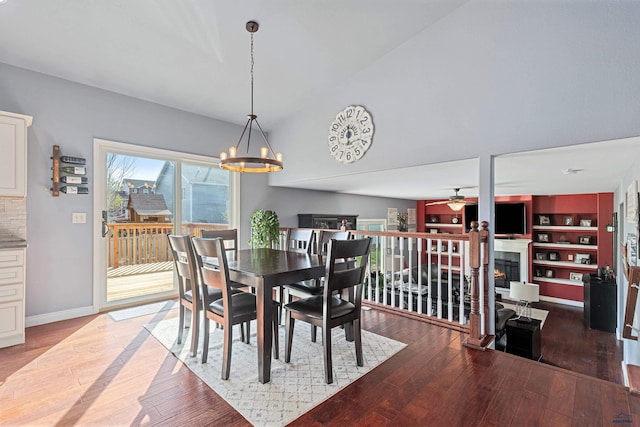 dining space with light wood finished floors, a warm lit fireplace, built in features, baseboards, and ceiling fan with notable chandelier