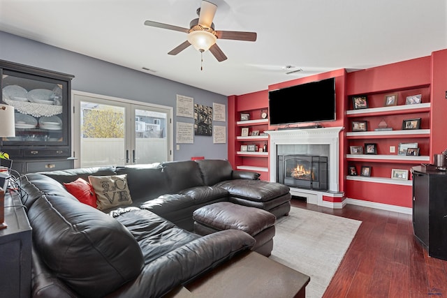 living room featuring dark wood-style floors, a tiled fireplace, ceiling fan, built in features, and visible vents