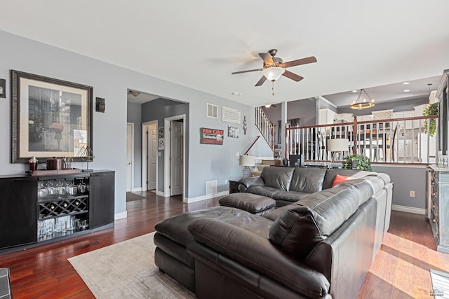 living room featuring visible vents, wood finished floors, ceiling fan with notable chandelier, baseboards, and stairway