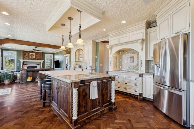 kitchen featuring stainless steel refrigerator with ice dispenser, open floor plan, a center island with sink, and light stone countertops
