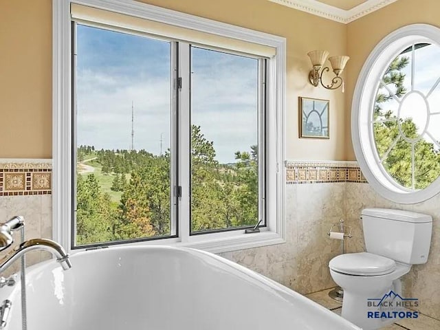 bathroom with toilet, tile walls, and a healthy amount of sunlight