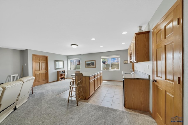 kitchen with a kitchen island, light carpet, open floor plan, a kitchen breakfast bar, and a sink