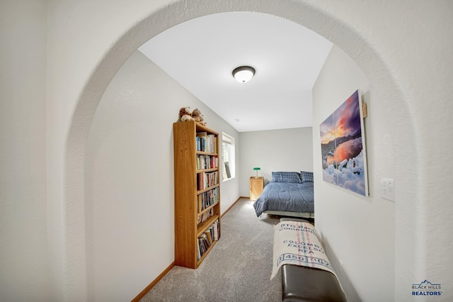carpeted bedroom with baseboards and arched walkways