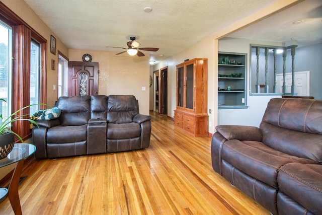 living room with light wood-type flooring, a ceiling fan, a textured ceiling, and built in shelves