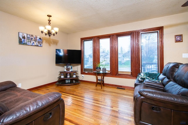 living room featuring visible vents, baseboards, a chandelier, and light wood finished floors
