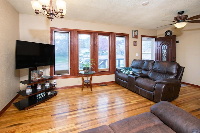 living room with a textured ceiling, ceiling fan with notable chandelier, baseboards, wood finished floors, and visible vents
