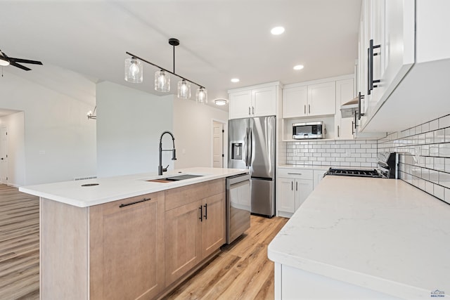 kitchen featuring appliances with stainless steel finishes, a sink, a ceiling fan, decorative backsplash, and light wood-type flooring