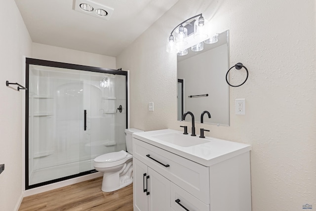 bathroom featuring a textured wall, vanity, toilet, a shower stall, and wood finished floors