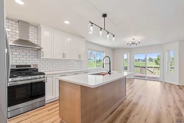 kitchen with wall chimney range hood, backsplash, stainless steel range with gas stovetop, a sink, and light countertops