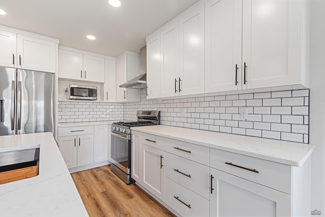 kitchen with wall chimney range hood, white cabinetry, appliances with stainless steel finishes, and recessed lighting
