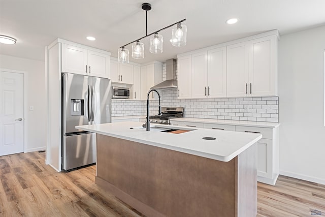 kitchen with wall chimney range hood, appliances with stainless steel finishes, light wood-type flooring, light countertops, and white cabinets