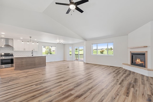 unfurnished living room with ceiling fan, a sink, high vaulted ceiling, a glass covered fireplace, and light wood-style flooring