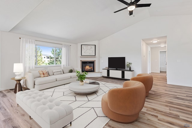 living area with a glass covered fireplace, lofted ceiling, baseboards, a ceiling fan, and light wood-style flooring